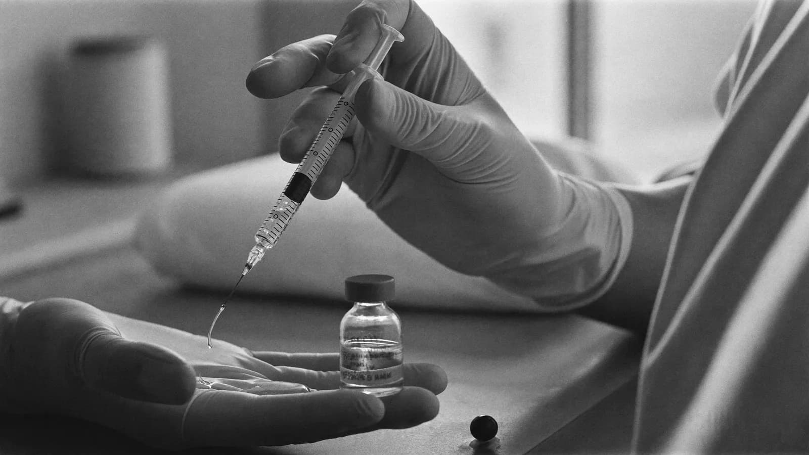 Gloved hands holding a syringe of clear hyaluronic acid gel beside a glass vial