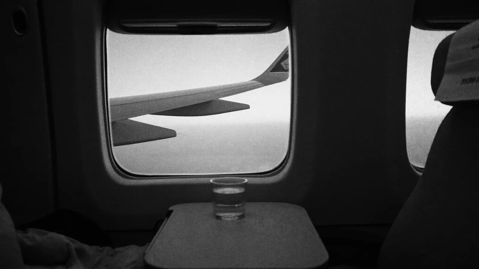 An aircraft window at dawn with a glass of water on the tray table