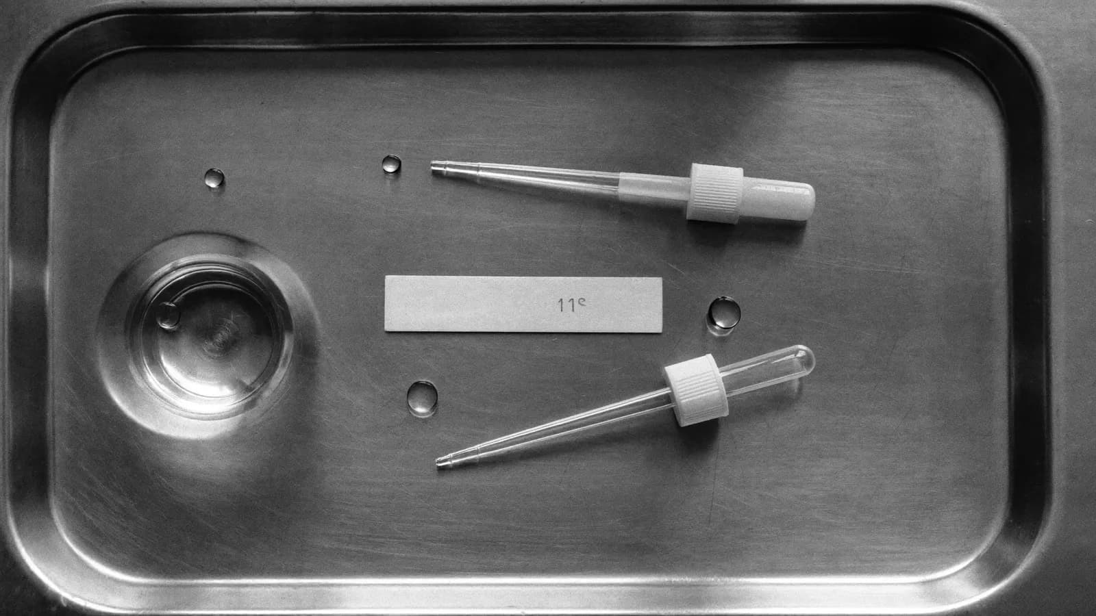 A clinical sample cup and a test strip on a steel tray by a window